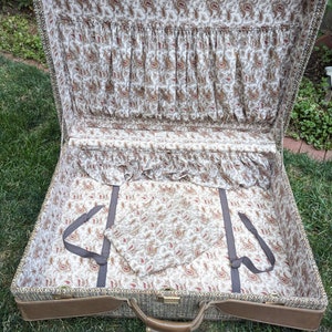 May include: An open vintage suitcase with a brown tweed exterior and a paisley patterned lining. The suitcase has a brown leather handle and a brass latch.