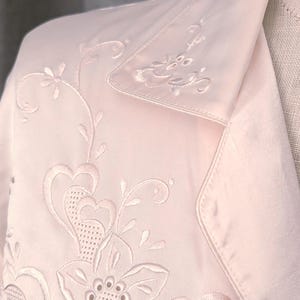 May include: Pale pink satin jacket with detailed floral embroidery. The jacket has a notched collar and embroidered flowers and leaves. The embroidery is in a matching pale pink thread, creating a delicate and elegant appearance.