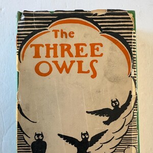 May include: Vintage book cover for "The Three Owls" featuring a cream-colored background with black and orange text and illustrations. The cover has three black owl silhouettes, a tree branch, and a small building.