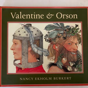 May include: A book cover with the title "Valentine & Orson" in white lettering. The illustration features two side profiles of people, one wearing a helmet and the other with a beard made of leaves and berries. The author's name, Nancy Ekholm Burkert, is at the bottom.