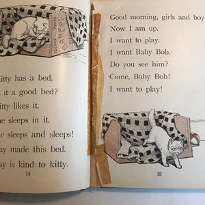 May include: A black and white illustration of a cat sleeping in a bed. The cat is white with black markings. The bed is made of wood and has a checkered blanket. The text "Kitty has a bed. Is it a good bed? Kitty likes it. She sleeps in it. She sleeps and sleeps! May made this bed. May is kind to kitty." is printed below the image. The page number "14" is printed at the bottom of the page.