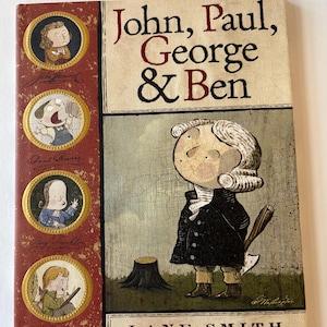 Może przedstawiać: Twarda oprawa książki zatytułowana "John, Paul, George & Ben" autorstwa Lane Smith. Okładka zawiera ilustracje postaci historycznych i postać z kreskówki z siekierą. Grzbiet książki jest czerwony z portretami w złotych ramkach.