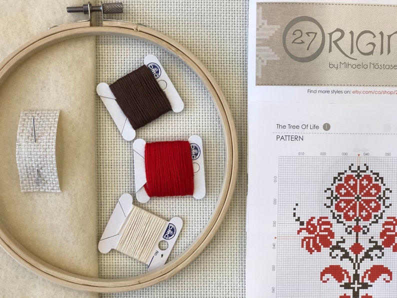 May include: Cross-stitch supplies including a wooden embroidery hoop, three spools of thread in brown, red, and cream, and a piece of fabric with a needle. A pattern sheet with the text "The Tree Of Life" is also visible.
