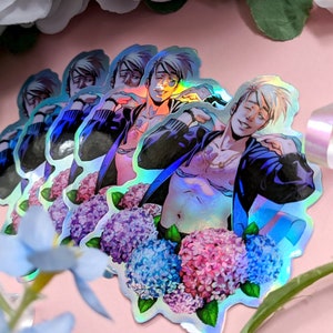 May include: Holographic stickers featuring a male anime character with blonde hair and a partially unbuttoned jacket. The stickers are surrounded by a floral arrangement of blue, pink, and purple hydrangeas. The background is a soft pink.