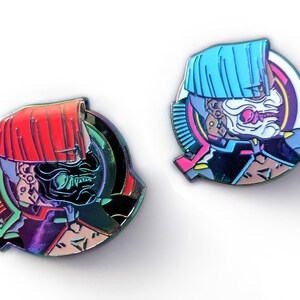 Könnte beinhalten: Zwei Emaille-Anstecknadeln mit einem stilisierten, futuristischen Samurai-Design. Eine Nadel hat einen roten Helm, die andere einen blauen Helm. Beide Nadeln haben eine schwarze Maske und eine lebendige Farbpalette mit schillernden Akzenten. Die Anstecknadeln sind kreisförmig und detailliert.