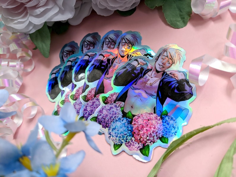 May include: Holographic stickers featuring a male anime character with blonde hair and a partially unbuttoned jacket. The stickers are surrounded by a floral arrangement of blue, pink, and purple hydrangeas. The background is a soft pink.