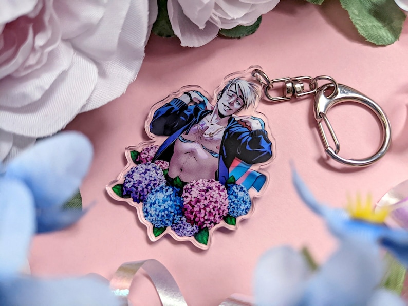 May include: A clear acrylic keychain featuring a stylized illustration of a person with white hair and a blue jacket. The person is surrounded by blue, purple, and pink hydrangeas. The keychain has a silver clasp.