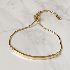 以下が含まれることがあります： 湾曲したバーチャームが付いたゴールドの調節可能なブレスレット。ブレスレットは、細い編み込みチェーンで作られています。