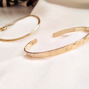May include: Two gold bracelets, one with a smooth finish and the other with a hammered texture.