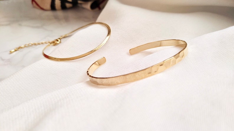 May include: Two gold bracelets, one with a smooth finish and the other with a hammered texture.