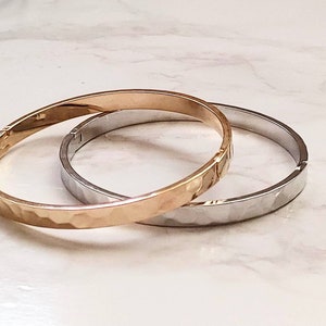 May include: Two hammered metal bangles, one gold and one silver, stacked on top of each other.