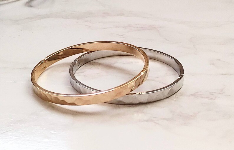 May include: Two hammered metal bangles, one gold and one silver, stacked on top of each other.