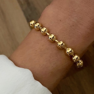 May include: A gold beaded bracelet with a chain link design. The bracelet is worn on a person's wrist.