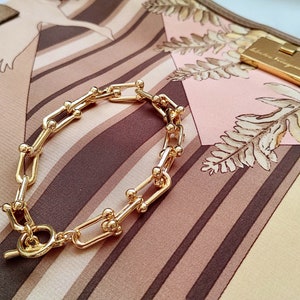 May include: A gold chain bracelet with a toggle clasp. The bracelet is made of linked, rectangular shapes with small round accents.