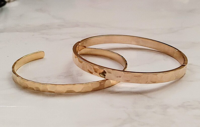 May include: Two gold-toned hammered metal bangle bracelets. The bracelets are stacked on top of each other.