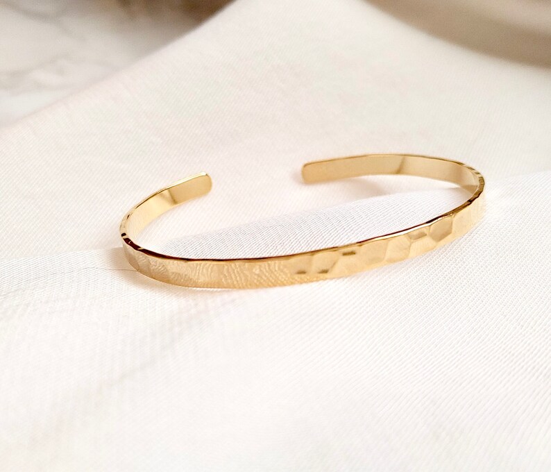 May include: A gold hammered bangle bracelet. The bracelet is simple and minimalist, with a smooth, polished finish.