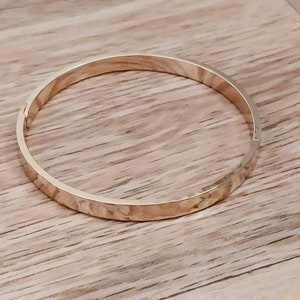 May include: A gold-toned bangle bracelet with a hammered texture.