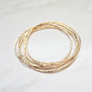 Puede incluir: Un conjunto de cinco pulseras de brazalete doradas con textura martillada.