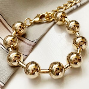 May include: A gold bracelet with a chain link and round beads. The beads are large and shiny.