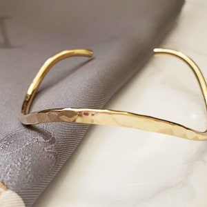 May include: A gold hammered bangle bracelet. The bracelet is simple and elegant, with a smooth, polished finish.