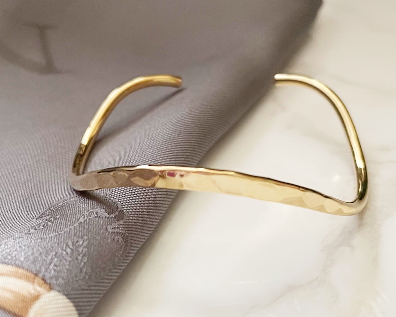 May include: A gold hammered bangle bracelet. The bracelet is simple and elegant, with a smooth, polished finish.