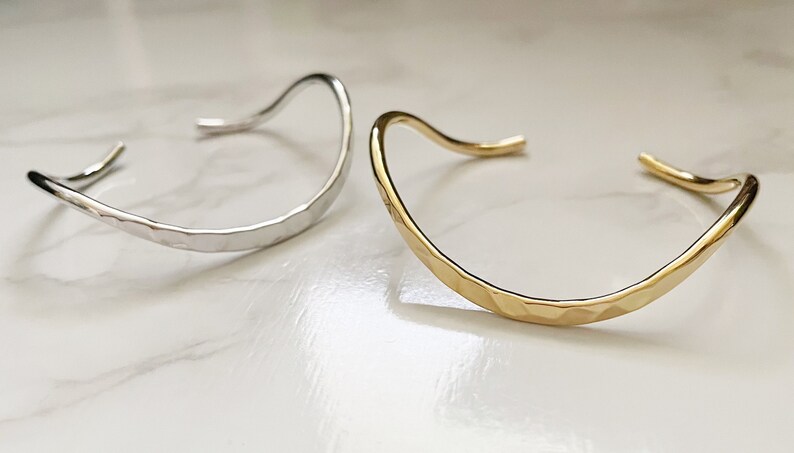May include: Two hammered metal bangles, one silver and one gold, with a curved, open design.