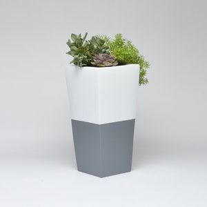 May include: A white and gray planter with a variety of succulents. The planter is tall and has a square shape.