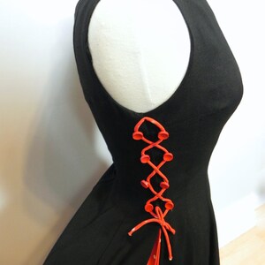 May include: A sleeveless black dress featuring a side lace-up detail with bright orange buttons and matching orange cord lacing. The side opening reveals a red fabric panel with white polka dots underneath the lacing and a tied cord at the base.
