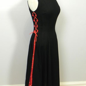 May include: A sleeveless black dress featuring a side panel with red and white polka dot fabric. The side is accented with red lacing threaded through red buttons, creating a decorative crisscross pattern that runs down the length of the bodice.