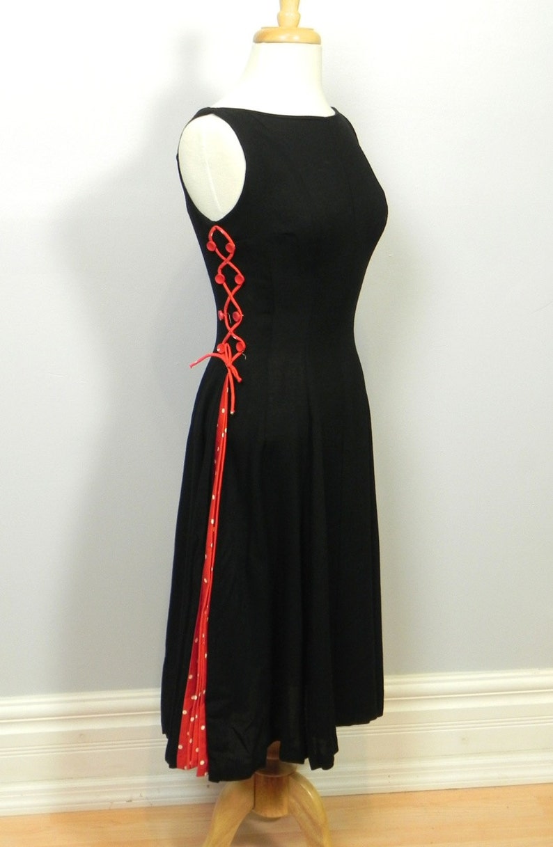May include: A sleeveless black dress featuring a side panel with red and white polka dot fabric. The side is accented with red lacing threaded through red buttons, creating a decorative crisscross pattern that runs down the length of the bodice.