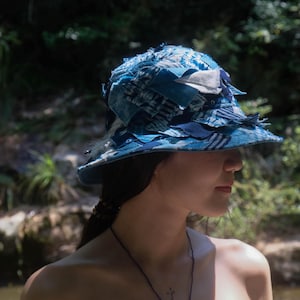 以下が含まれることがあります： フリンジの付いた青と白のパッチワークのバケットハット。帽子は、異なる生地を縫い合わせて作られています。