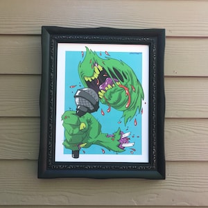 May include: A framed art print featuring a green monster with a microphone. The monster has a large mouth and is dripping with red liquid. The art is set against a light blue background and is framed in a black ornate frame.