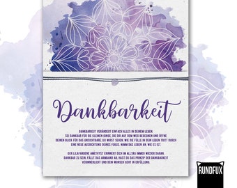 May include: A rectangular card featuring a purple watercolor mandala design at the top and the German text "Wunscharmband" and "Dankbarkeit" printed in purple. A thin black string bracelet is attached horizontally across the center of the card.