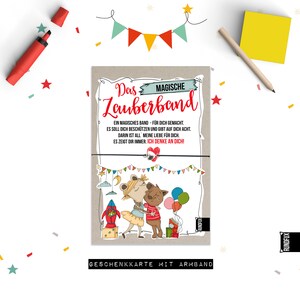 May include: A colorful card with a cartoon illustration of two animals hugging. The card says "Das Magische Zauberband" and "Ein magisches Band - für dich gemacht. Es soll dich beschützen und gibt auf dich acht. Darin ist all meine Liebe für dich. Es zeigt dir immer: Ich denke an dich!"  The card also says "Geschenkkarte mit Armband".