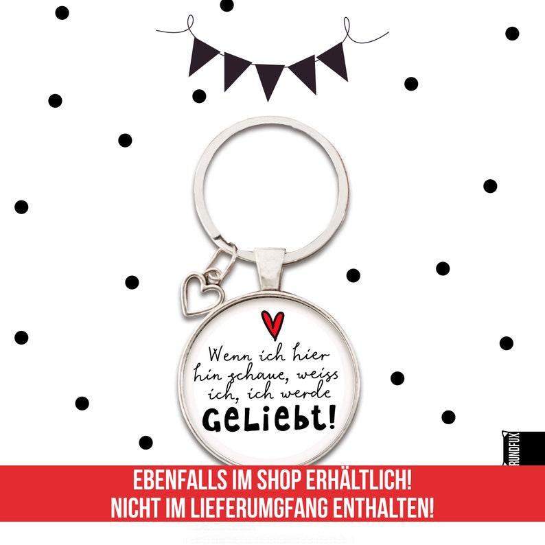 May include: A silver keychain with a round glass charm that says "Wenn ich hier hin schaue, weiss ich, ich werde Geliebt!" in black text with a red heart. The charm is attached to a silver heart charm and a silver key ring.