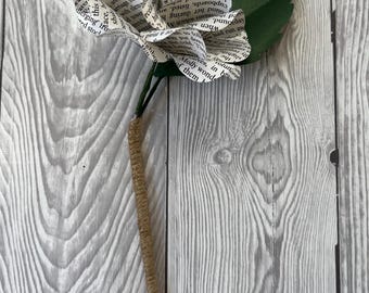Könnte beinhalten: Eine weiße Papierblume aus Buchseiten mit grünen Papierblättern. Die Blume ist an einem braunen Bindfaden befestigt.