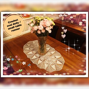 Könnte beinhalten: Ein cremefarbenes, ovales Häkeldeckchen oder ein kleiner Tischläufer wird auf einem Holztisch präsentiert. Eine klare Glasvase enthält einen Strauß rosa und gelber Blumen. Der Text im Bild lautet "Crochet oval doily / small table runner."