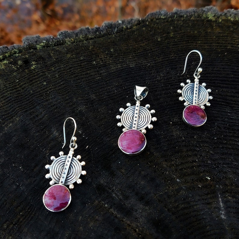 May include: A set of silver earrings and a pendant with a pink stone and a circular design.