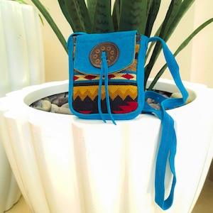Könnte beinhalten: Eine kleine blaue Umhängetasche mit einem geometrischen Muster in Rot, Gelb und Schwarz. Die Tasche hat einen Klappenverschluss mit einem braunen Lederakzent und einem Metallknopf.
