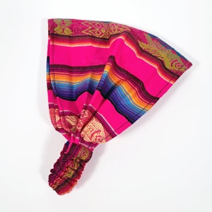 May include: A pink and multi-colored striped headband with a woven pattern. The headband is tied at the back with a knot.
