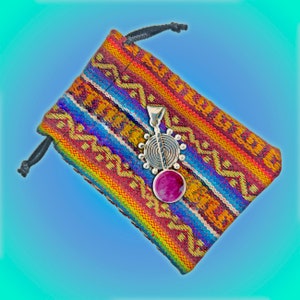 May include: A silver pendant with a pink stone and a circular design hangs in a colorful woven pouch.