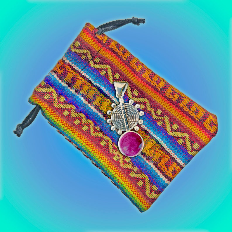 May include: A silver pendant with a pink stone and a circular design hangs in a colorful woven pouch.