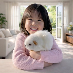 May include: A young person wearing a light pink sweater holds a fluffy, white pet with brown markings. The pet is small and round, with soft-looking fur. The background includes a bright, open doorway and a glimpse of a living room.