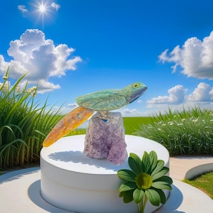 May include: A green and yellow carved stone sculpture of a bird perched on a purple amethyst crystal. The sculpture is on a white pedestal against a blue sky with white clouds.