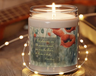 May include: A beige candle with a floral design and a quote about pleasures being like poppies. The candle is lit and sitting on a wooden coaster.