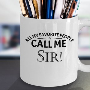May include: White ceramic mug with a black design that says "All my favorite people call me Sir!" The mug has a handle and is filled with pens.