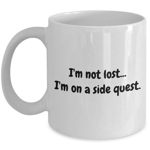 May include: White ceramic coffee mug with black text that reads "I'm not lost... I'm on a side quest."