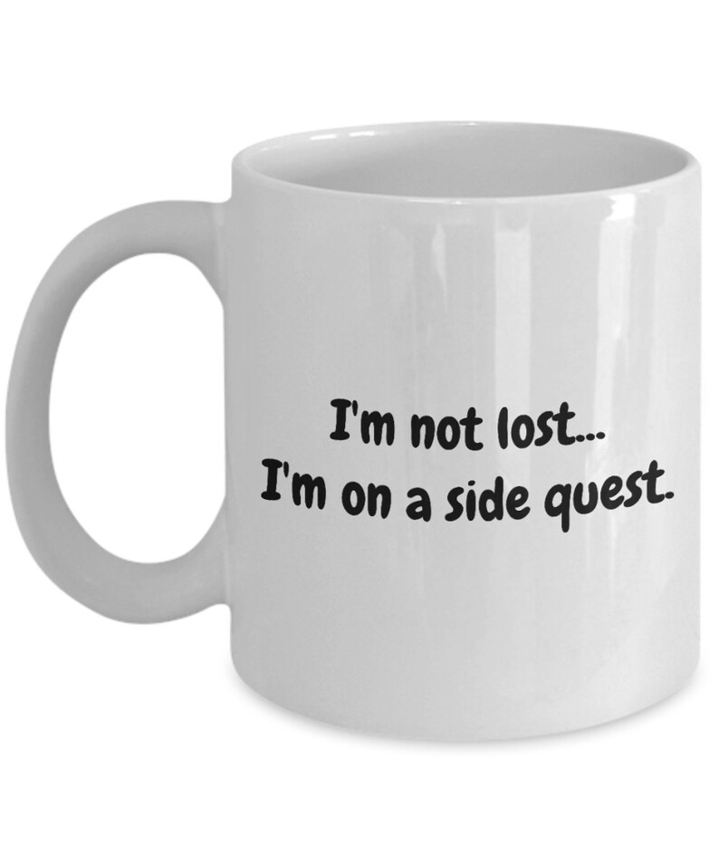May include: White ceramic coffee mug with black text that reads "I'm not lost... I'm on a side quest."