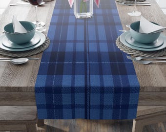 May include: Blue and black plaid table runner with a woven texture. The runner is laid out on a wooden table with place settings.