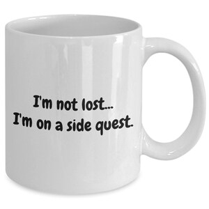 May include: White ceramic coffee mug with black text that reads "I'm not lost... I'm on a side quest."